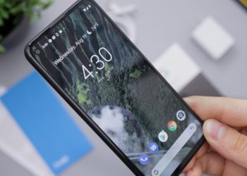 Android phone held in a hand while displaying the home screen