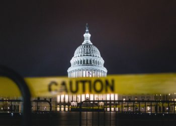 Picture of the U.S. Capitol building lit up at night. In the foreground of the image is a blurred yellow 'Caution' tape, which hides part of the building in the background.