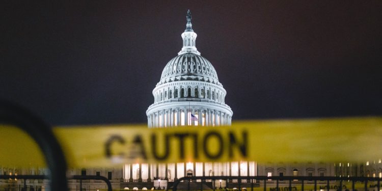 Picture of the U.S. Capitol building lit up at night. In the foreground of the image is a blurred yellow 'Caution' tape, which hides part of the building in the background.
