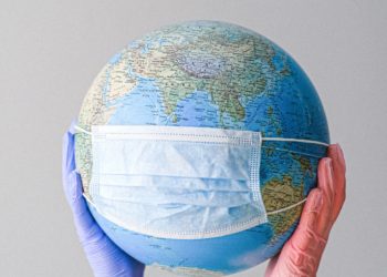 Two gloved hands holding up a globe wearing a surgical mask