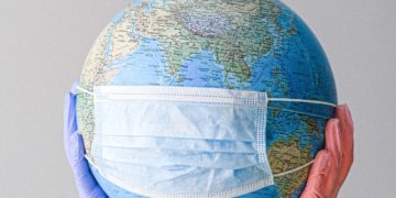 Two gloved hands holding up a globe wearing a surgical mask