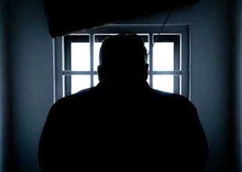 Silhouette of a man facing a barred window.