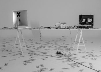 black and white image of a macbook computer screen - from the back - and an open suitcase. There are dollar bills all over the floor