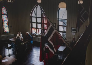 Room with Norwegian flags mounted on the wall and people in the background