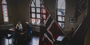 Room with Norwegian flags mounted on the wall and people in the background