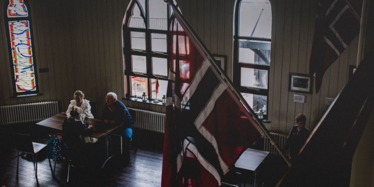 Room with Norwegian flags mounted on the wall and people in the background