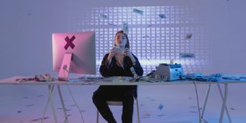 Woman sitting by computer with lots of cash around her - cybercriminal