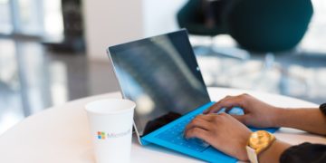 Person using blue laptop next to coffee cup