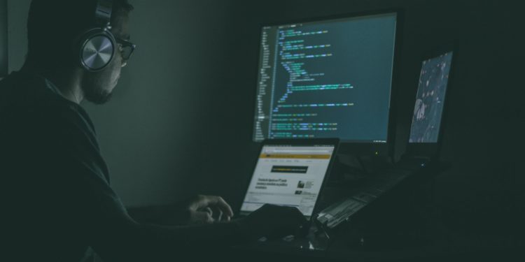Dark room with person sat at two screens