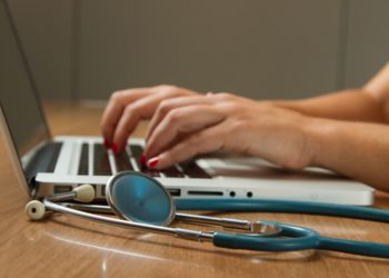 stethoscope next to laptop. Fingers typing.