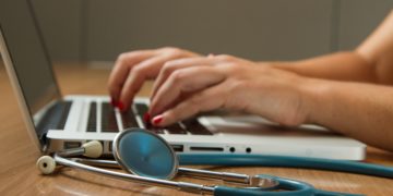 stethoscope next to laptop. Fingers typing.