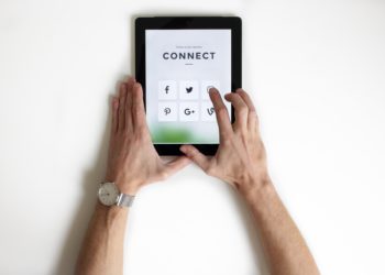 Electronic tablet with social media icons, hands holding screen.