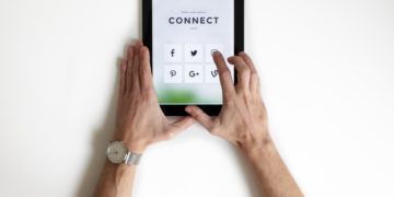 Electronic tablet with social media icons, hands holding screen.