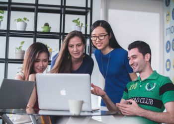 Four people huddle around a computer in an office type space.