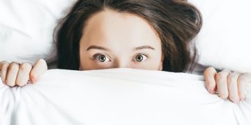 Woman hiding under bed sheet